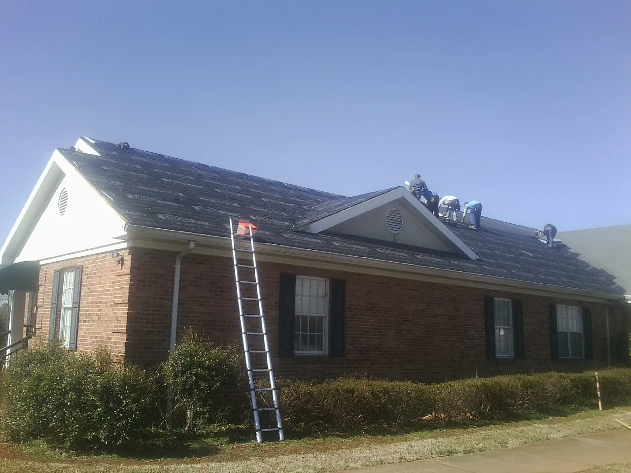 Crew tearing shingles off a brick ranch roof with a ladder set — Metal Roof Repair work by our crew in Nixon
