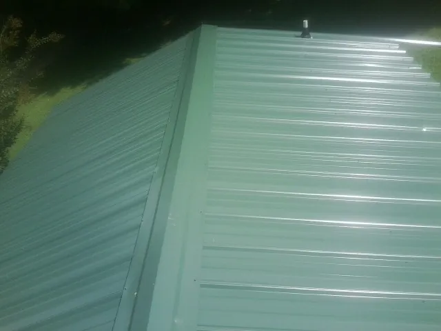 New green metal panels meeting at the ridge of a roof — Flat Roof Repair work by our crew in Nixon