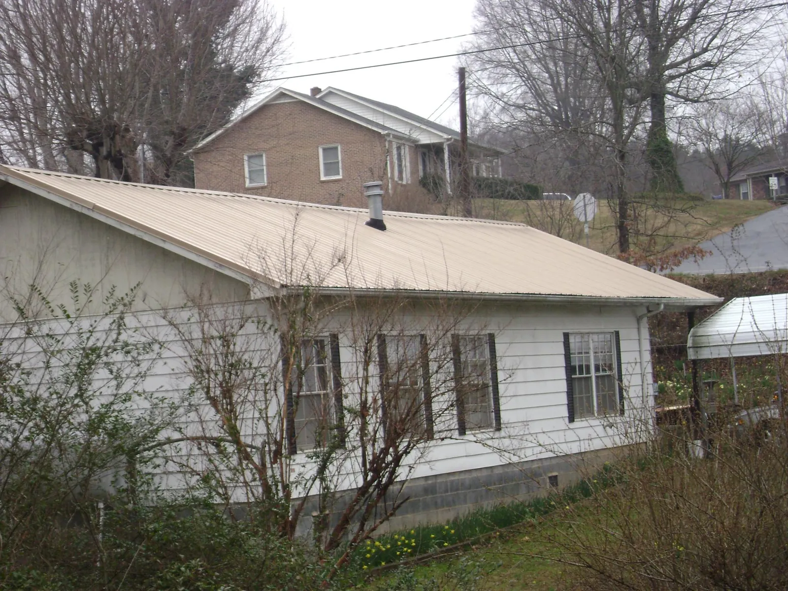 Tan metal roof on a white sided house set into a hillside — Commercial Roofing by Roofing Brothers in Nixon
